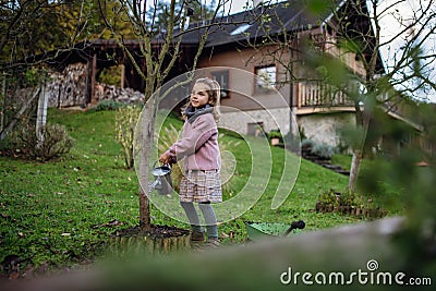 Little girl watering tree in garden, using collected rainwater. Concept of water conservation in garden and family Stock Photo