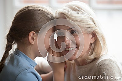 Little girl whisper in ear tell secret to curious grandmother Stock Photo