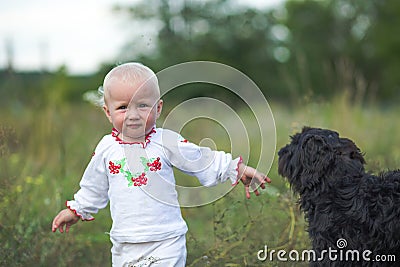 little girl in white clothes plays with black dog. Communication of children and animals. Good home dog outdoor Stock Photo