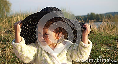 Little girl in a white terry robe tries on a black sun hat Stock Photo