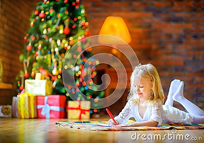 Little girl writes a letter to santa lying on the floor near Christmas tree Stock Photo