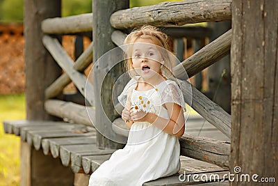 Little girl 5 years blonde sitting on a log home, holding hands Stock Photo