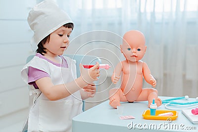 Little girl 3 years old preschooler playing doctor with doll. The child makes an injection toy. Stock Photo