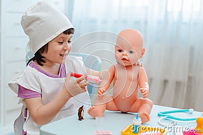 Little girl 3 years old preschooler playing doctor with doll. The child makes an injection toy. Stock Photo