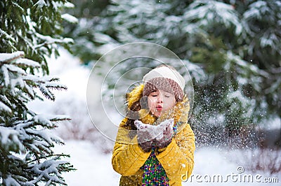 A little girl in a yellow jacket plays with snow in the winter. The child holds the snow in his hands Stock Photo