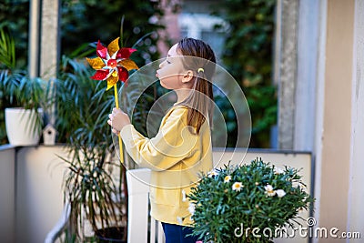 Little girl in a yellow sweatshirt on the balcony blowing on a windmill Stock Photo