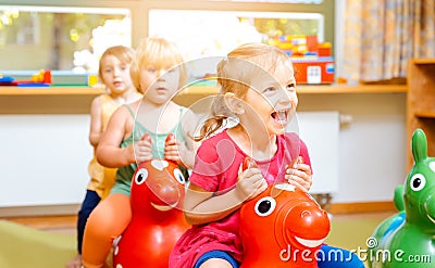 Little girls riding on play horses in kindergarten Stock Photo