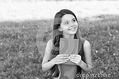 Little happy girl reading book outdoors sunny day, daydreamer concept Stock Photo