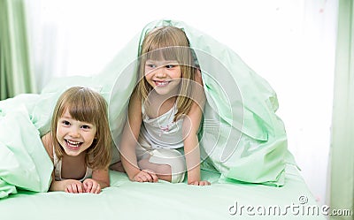 Little happy girls lying under blanket on bed Stock Photo