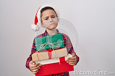 Little hispanic boy wearing christmas hat holding presents skeptic and nervous, frowning upset because of problem Stock Photo