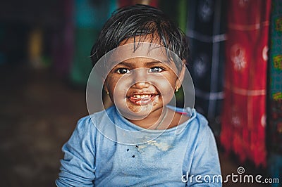 A little Indian girl looks at the camera and smiles at the photographer. Chocolate baby. Indian child in old clothes. Portrait of Editorial Stock Photo