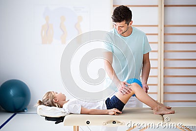 Little injure girl on massage table exercising with young male doctor Stock Photo