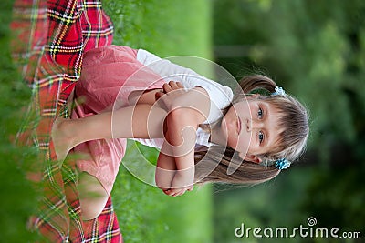 Little irritated girl sitting on plaid in grass Stock Photo