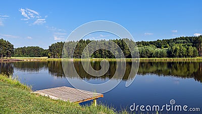 Little jetty standing next to the lake. Calm and still surface of the water. Hills covered with forest in the background. Jacnia, Stock Photo