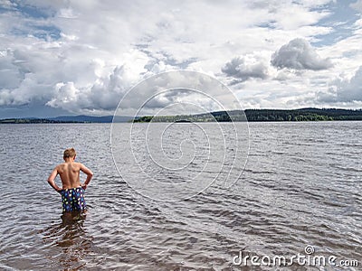 Little joyful Caucasian funny boy try cold water of lake Stock Photo