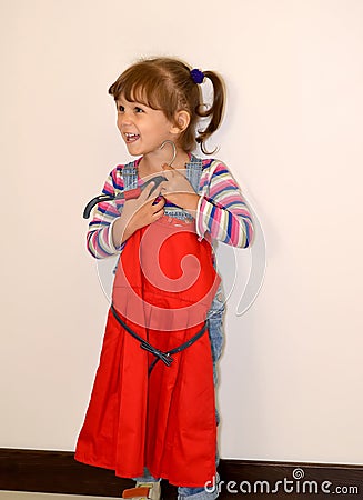 The little joyful girl tries on a beautiful red dress Stock Photo