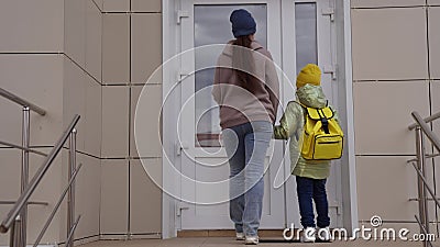 a little kid with a backpack goes with his mother hand in hand to school. little kid and mom rush to the school lesson Stock Photo