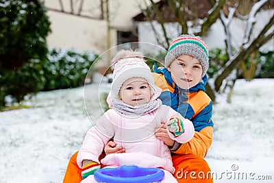 Little kid boy and cute toddler girl sitting together on sledge. Siblings, brother and baby sister enjoying sleigh ride Stock Photo