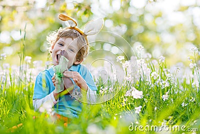 Little kid boy eating chocolate Easter bunny outdoors Stock Photo