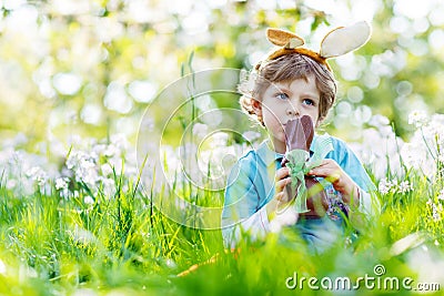 Little kid boy eating chocolate Easter bunny outdoors Stock Photo