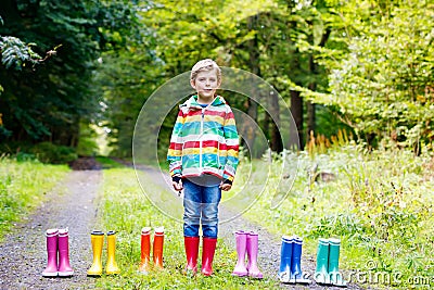 Little kid boy and group of colorful rain boots. Blond child standing in autumn forest. Close-up of schoolkid and Stock Photo