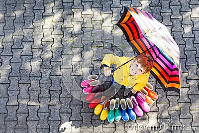 Little kid boy and group of colorful rain boots. Blond child standing under umbrella. Stock Photo