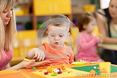 Little kid boy learning to use colorful play clay in kindergarten. Babies group studying in creche Stock Photo