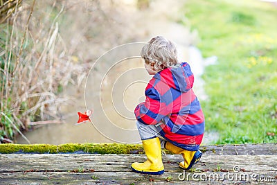 Little kid boy playing with paper ship by creek Stock Photo