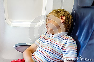 Little kid boy sleeping during long flight on airplane. Child sitting inside aircraft by a window Stock Photo