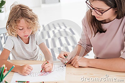 Little kid drawing a house using colorful crayons with his female, therapist during a meeting in the office Stock Photo