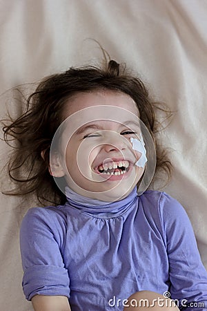 Little kid girl after accident with adhesive band on face laughing. Stock Photo