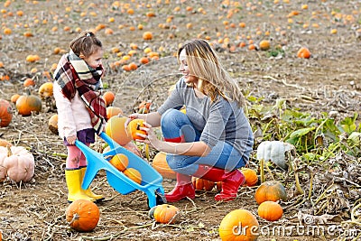 Little kid girl and beautiful mother having fun with farming on a pumpkin patch. Traditional family festival with Stock Photo