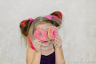 A little kid girl dabbles and plays with two fresh donuts before eating. A child holds donuts near his eyes and looks through the Stock Photo