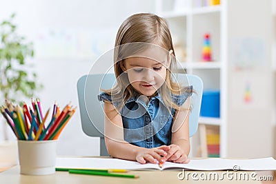 Little kid girl draws sitting at table in room in nursery Stock Photo