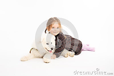 Little kid girl in dress looking at the camera, child hugging her samoyed puppy while liying on the ground Stock Photo