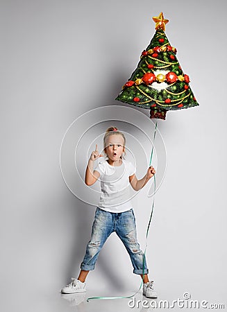 Kid girl in jeans, t-shirt with christmas tree air balloon is showing attention important sign on white with copy space. Stock Photo