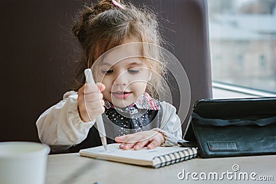 Little kid girl writing or drawing with pen in scetch book Stock Photo