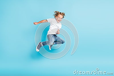 Little kid jump motion funny grimace hands wear white shirt jeans sneakers isolated blue color background Stock Photo