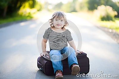 Little kid sitting on a suitcase outdoors, ready for the journey Stock Photo