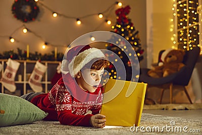 Little boy opens magic book and reads wonderful stories and fairy tales on Christmas Eve at home Stock Photo