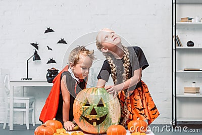 little kids in halloween costumes near table with pumpkins Stock Photo