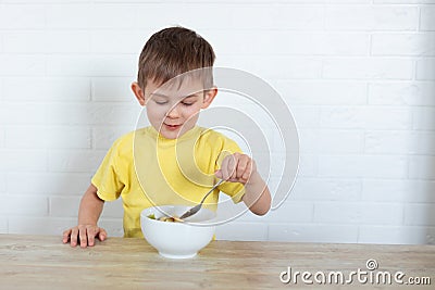 Little left-handed boy in a yellow T-shirt eating fruit salad and smiling. Children healthy food concept. Nutrition Stock Photo