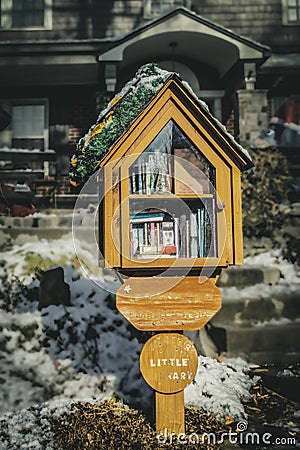 Little library in neighborhood on pole in front yard with Christmas decorations in front of house with snow on ground Stock Photo