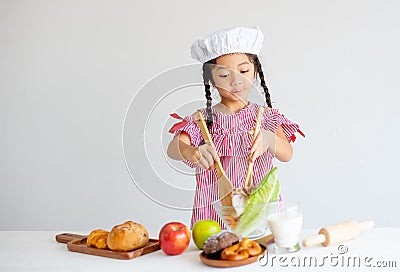 Little lovely girl use ladle to mix salad in glass bowl on table and she look enjoy with this activity Stock Photo