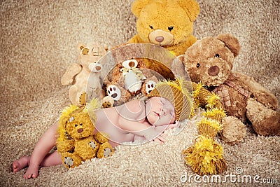 Little newborn baby in a knitted cap sleeping near teddy bears toys. Stock Photo