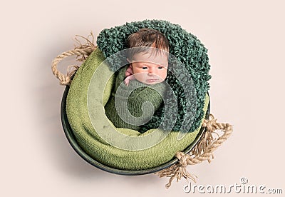 Nwborn swaddled in green coccon lying on basket Stock Photo