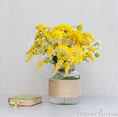 Little old book, a bouquet of flowers chrysanthemums, goldenrod and daisies in a glass vase homemade Stock Photo