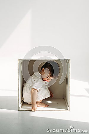A little one-year-old girl is playing, climbed into a wooden cube - a chair Stock Photo
