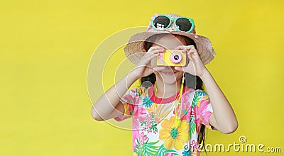 Little photographer taking photo by toy camera. Child tourists in floral pattern summer dress and hat with sunglasses isolated on Stock Photo