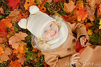 Little pretty girl in a beige coat lying on the leaves in autumn Stock Photo